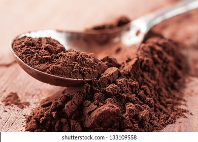 Brown chocolate powder on a spoon over a wooden table