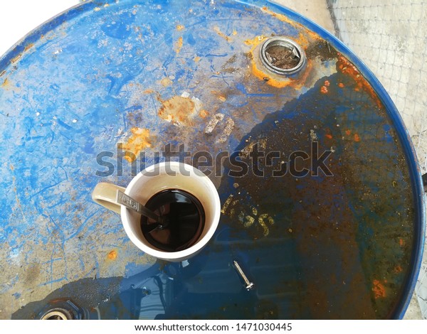 Brown Coffee cup is placed on a blue oil\
tank.It\'s a drink of a mechanic in a car\
garage.