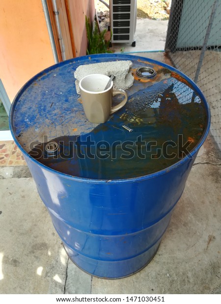 Brown Coffee cup is placed on a blue oil\
tank.It\'s a drink of a mechanic in a car\
garage.