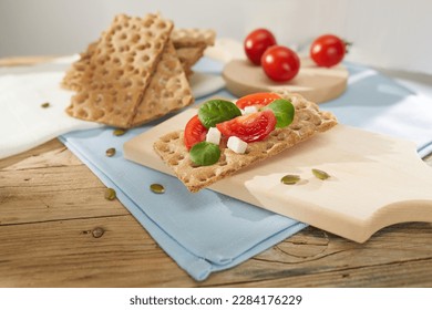 panecillos marrones con tomates y queso en una tabla de madera. aperitivo saludable con pan de cereales. desayuno en un día soleado. pan crujiente relleno de verduras