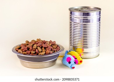 Brown Crunchy Organic Kitty Kibble Pieces In A Bowl, Toy Mice And Wet Cat Food In Metal Can For Pet Feed On Light Background