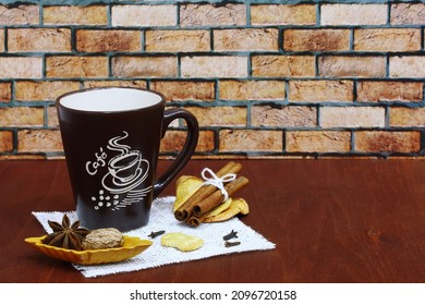 A brown cup with coffee, cinnamon, dried fruits, nutmeg and anise on a wooden table against a brick wall. Closeup, still life, negative space on the right. - Shutterstock ID 2096720158