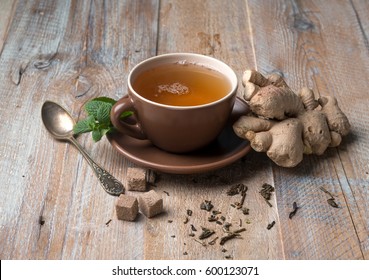 Brown cup of ginger tea with cubes of brown sugar, aged spoon, giner on side