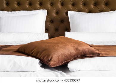 Brown cushion lying on a throw rug over a white duvet on a stylish double bed with upholstered brown headboard, close up view - Powered by Shutterstock