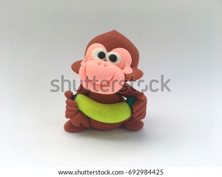 Brown cute and lovely cartoon clay monkey smile is lifting yellow banana on hand in white background in concept enjoy ,happy,naughty ,healthy ,exercise