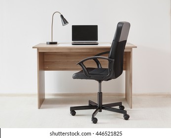 Brown desk with laptop lamp and office chair isolated near the wall.