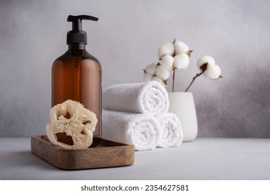 Brown dispenser bottle, loofah sponge and white towels. Set of bathroom accessories. 