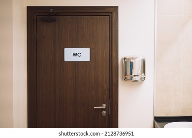 brown door in a public toilet with a sign WC and a hand dryer. 