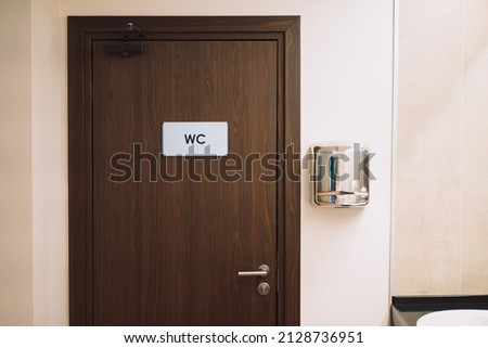 brown door in a public toilet with a sign WC and a hand dryer. 