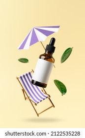 Brown Dropper Glass Bottle, Beach Chair, And Sunshade Flying In Antigravity On Pastel Yellow Background. Levitation Objects In The Air. Skincare Concept. Organic Natural Cosmetic Product. Mockup