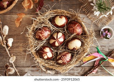 Brown Easter egg dyed with onion peels with a pattern of fresh leaves in a wicker basket, top view