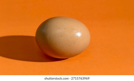 Brown egg on orange surface with shadow, highlighting simplicity, texture, and minimalist composition.
