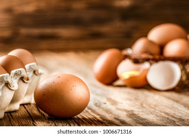 Brown eggs in carton box. Broken egg with yolk in background. 