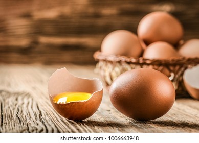 Brown Eggs In Wooden Basket. Broken Egg With Yolk In Front. 