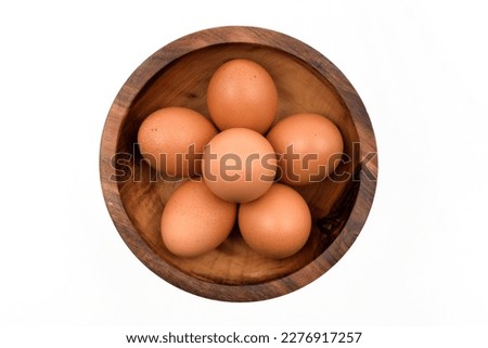 Brown eggs in a wooden bowl, isolated on white background, top view