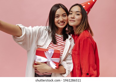 Brown Eyed Girls In Stylish Oversized Shirts Take Selfie, Smile, Hold Red Gift Box And Celebrate Birthday On Pink Background.