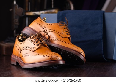 Brown full grain leather brogues on wooden display in in men shoes boutique store with box and cloth shoe bags.