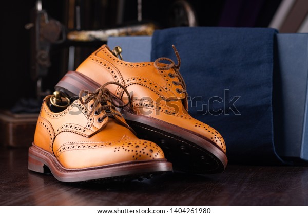 Brown full\
grain leather brogues on wooden display in in men shoes boutique\
store with box and cloth shoe\
bags.