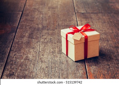 Brown Gift Box And Red Ribbon With Tag On Wood Background With Space.