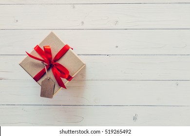 Brown gift box with tag on wooden background. Gift box with red ribbon on wood background with space. - Powered by Shutterstock