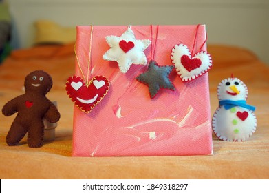
Brown gingerbread man, stars, hearts, and white snowman on a background of pink canvas. Handmade unique felt Christmas decorations