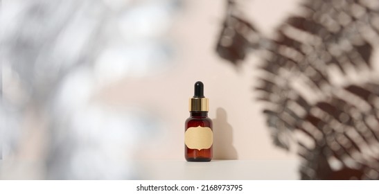 brown glass bottle with a pipette stands on a brown background. Container for cosmetics, serum and oil, silver fern leaf