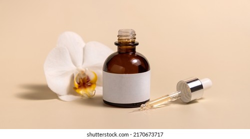 Brown glass dropper bottle near white orchid flowers on light yellow, close up, mockup. Skincare handmade beauty product, serum or lotion. Exotic natural cosmetics