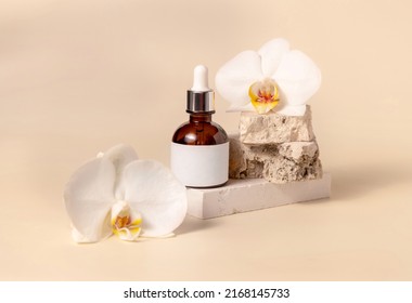 Brown glass dropper bottle on stone near white orchid flowers on light yellow, close up, mockup. Skincare handmade beauty product, serum or lotion. Exotic natural cosmetics