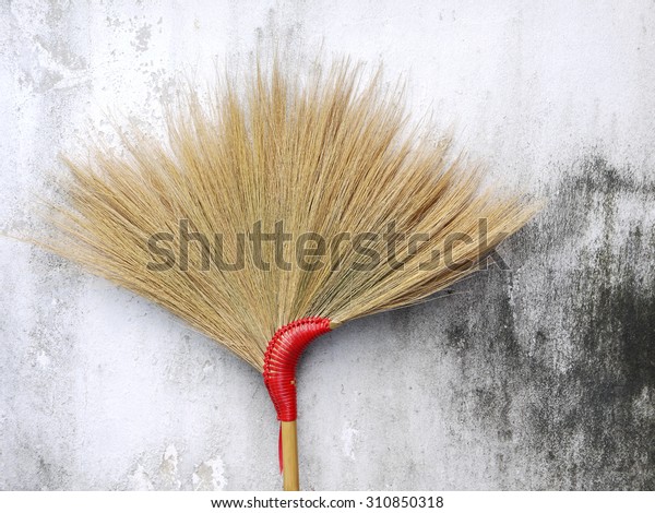 Brown grass broom on\
dirty white wall