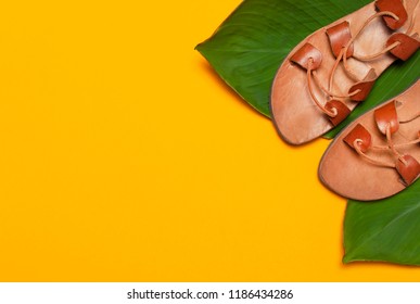 Brown Greek Leather Summer Sandals and tropical leaves on bright yellow minimalistic background. Womens shoes Summer festive background Top view Flat Lay with copy space