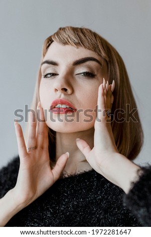 Brown hair woman in a black fluffy sweater touching her cheeks