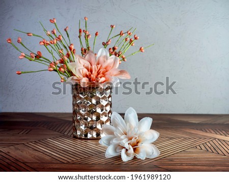 Brown hammered vase filled with peach dahlia artificial spring flowers and orange flower buds on a wooden table for a simple spring home decor.