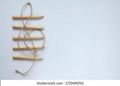 Brown hemp string treble clef and musical stave made of wooden coloured pencils on white background