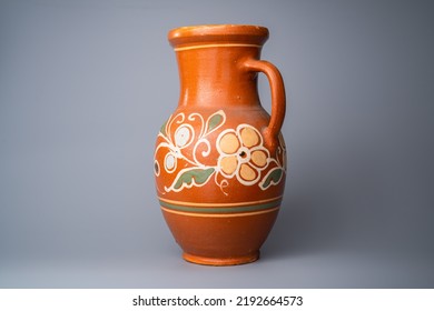 Brown Jug With Handle, Handmade From Clay With Floral Ornament On Orange Background In The Studio. Earthenware For Drink And Food. Kitchen Utensils. Old Rustic Cookware Made Of Earthen.