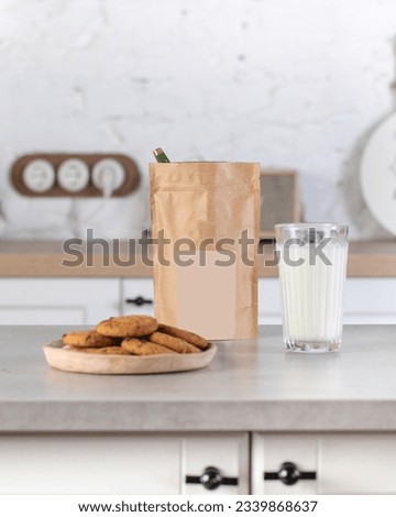 A brown kraft paper bag with a label layout on the kitchen table with a plate of cookies and a glass of milk. 