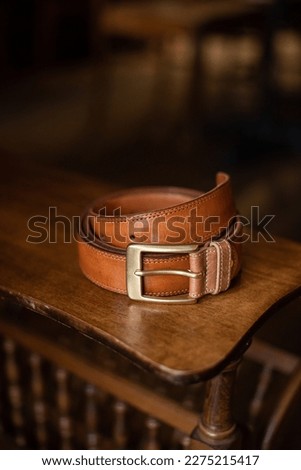 Brown leather belt with golden buckle on a wooden surface