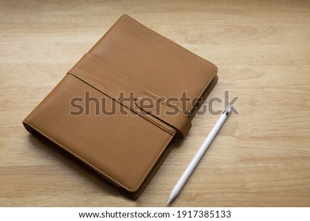 A brown leather notebook or planner and a pen on a wooden table