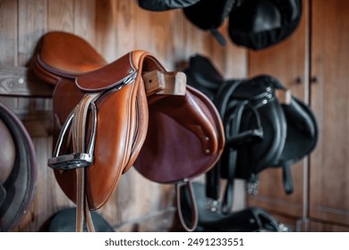 brown leather saddle hanging on wooden wall at stable or barn, professional equestrian horse riding equipment - Powered by Shutterstock