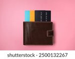 Brown leather wallet with colored plastic debit and credit bank cards on pink background, top view flat lay. Minimalistic concept of shopping, online payment. Stylish unisex wallet