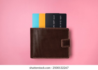 Brown leather wallet with colored plastic debit and credit bank cards on pink background, top view flat lay. Minimalistic concept of shopping, online payment. Stylish unisex wallet