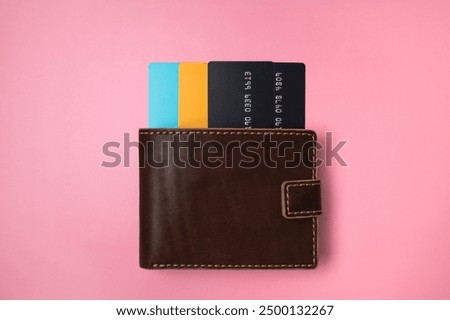 Brown leather wallet with colored plastic debit and credit bank cards on pink background, top view flat lay. Minimalistic concept of shopping, online payment. Stylish unisex wallet
