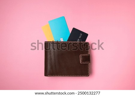 Brown leather wallet with colored plastic debit and credit bank cards on pink background, top view flat lay. Minimalistic concept of shopping, online payment. Stylish unisex wallet