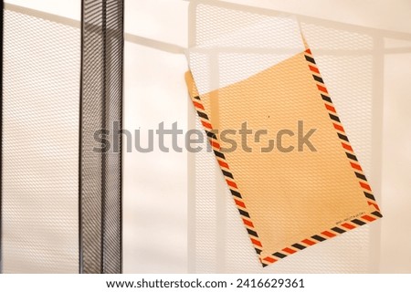 Brown letter envelope has a rectangular shape with colorful lines on the side which is usually called airmail. The envelope is exposed to the shadow of the steel wire.