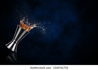 Brown Liquor Splashing Out Of A Jigger Isolated On Dark Blue Background	