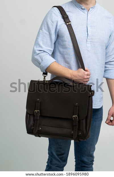 Brown men\'s shoulder leather bag for a\
documents and laptop on the shoulders of a man in a blue shirt and\
jeans with a white background. Satchel, mens leather handmade\
briefcase.