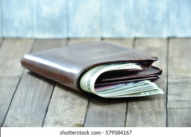 brown men's wallet and dollars on wooden background
