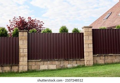 Brown metal profile fence with block posts. Incline construction. Corrugated surface. Security. Private property fencing. Opaque hedge. Outdoor house exterior. Side view. Urban or industrial style. - Shutterstock ID 2107248512