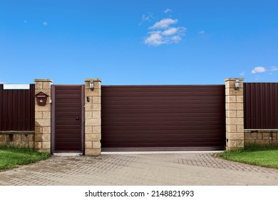 Brown metal profile fence with block posts. Entry group with gate, flashlight and postbox. Opaque surface, horizontal lines. Security. Private property fencing. Exterior. Pavement tiles on parking.