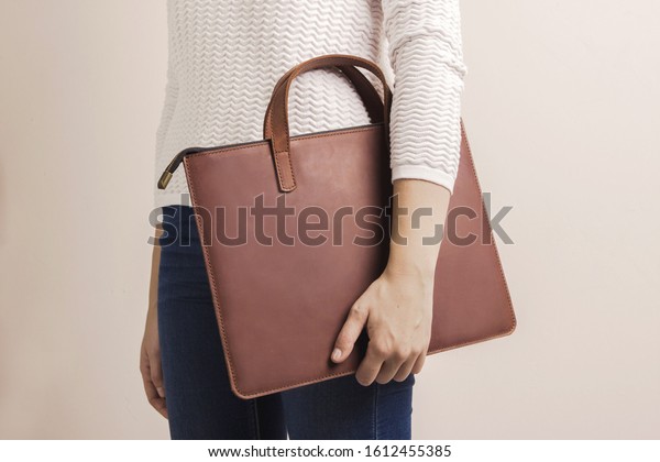 Brown modern\
unisex leather bag for laptop. Person holding case. Minimalist\
inclusion clothing concept\
