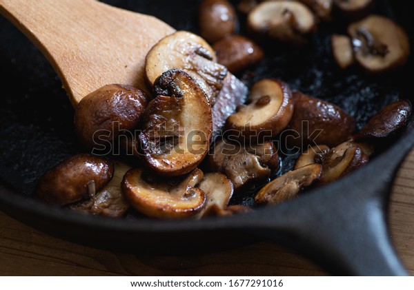 Brown mushrooms cooked in a cast iron skillet,\
wooden spatula.